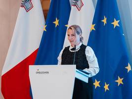 Namestnica varuha dr. Dijana Možina Zupanc za govorniškim pultom. V ozadju so zastave. 